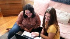 Two students sitting together on the floor looking at a laptop in a dorm room